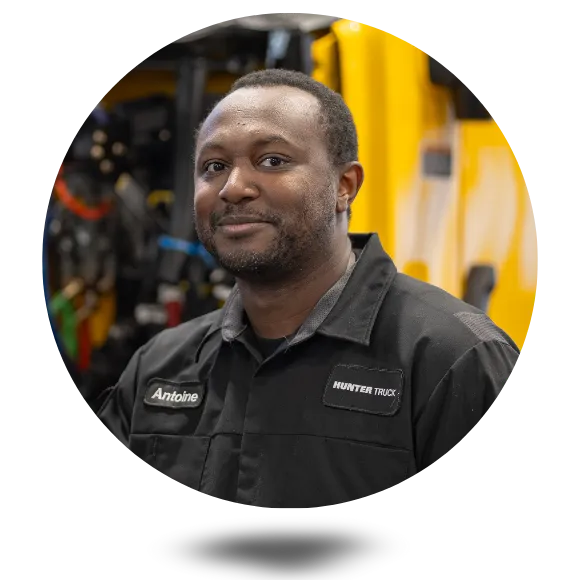 Young man, a peterbilt mechanic at hunter truck, stands in front of a peterbilt in a service bay.